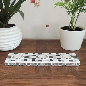 Peut inclure: Un bougeoir en mosaïque blanche avec trois puits de bougies. Le bougeoir est fait de petites tuiles blanches, noires et argentées.