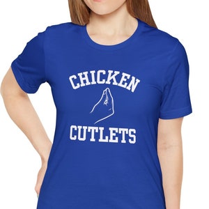 May include: A royal blue t-shirt with white text that reads "CHICKEN CUTLETS" and a white hand gesture above the word "CHICKEN".