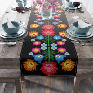 May include: A black table runner with a colorful floral pattern. The pattern features red, pink, yellow, blue, and green flowers. The runner is perfect for adding a touch of color to your dining table.