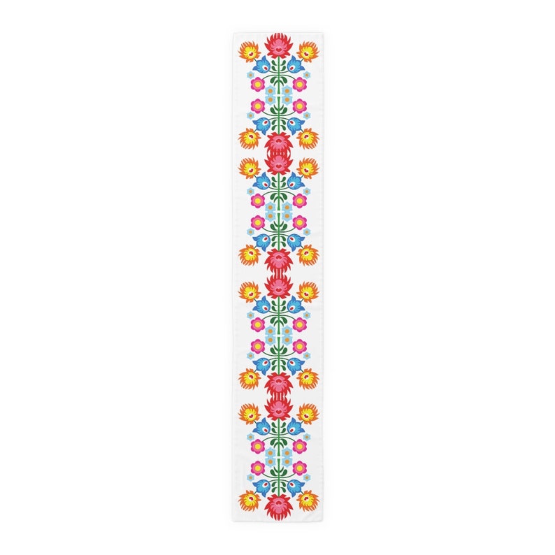 May include: A white table runner with a repeating pattern of colorful flowers. The flowers are red, orange, yellow, blue, and green. The pattern is symmetrical and creates a traditional folk art design.