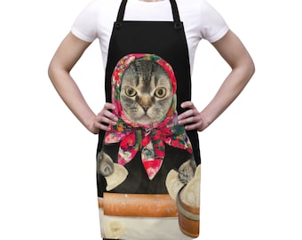 Puede incluir: Delantal negro con un gato que lleva un pañuelo rojo y floral y sostiene albóndigas. El gato está de pie frente a un rodillo y un tazón de albóndigas.
