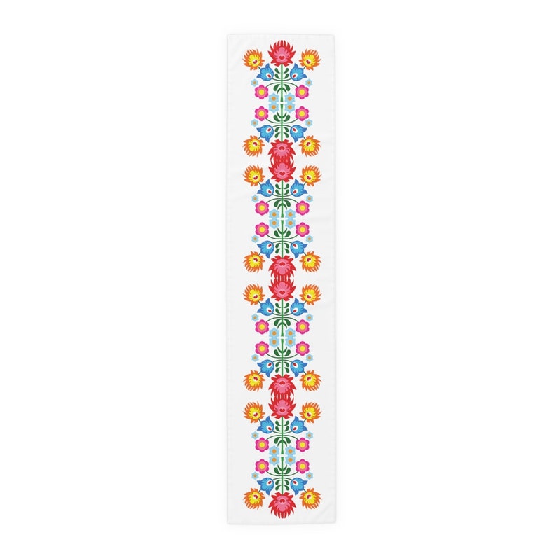 May include: A white table runner with a repeating pattern of red, orange, yellow, blue, and green flowers. The flowers are stylized and have a folk art design.