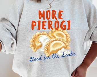 May include: A light gray sweatshirt with the words "MORE PIEROGI" in orange and a graphic of pierogi with sour cream. Below the graphic, the text reads "Good for the Soulie" in blue.