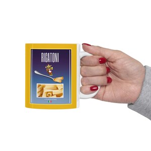 May include: White ceramic mug with a yellow border and a blue and white image of a box of pasta. The box says "Rigatoni" and "A Product of Italy".