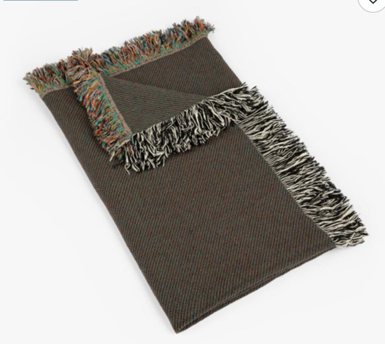 May include: A folded brown blanket with fringed edges. The fringe on one side is a mix of colors, while the other side has black and white fringe. The blanket is made of a woven material.