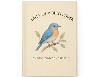Könnte beinhalten: Ein cremefarbenes Hardcover-Journal mit einer Illustration eines blauen Vogels auf dem Cover. Der Text "TALES OF A BIRD LOVER" steht über dem Vogel, mit "ASHLEY'S BIRD ADVENTURES" darunter.