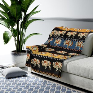 May include: A black and yellow throw blanket with a repeating pattern of stylized buffalo, rainbows, and geometric designs.