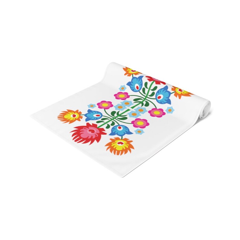 May include: White table runner with a colorful floral design. The flowers are red, pink, yellow, blue, and green. The design is a traditional Polish folk art pattern.