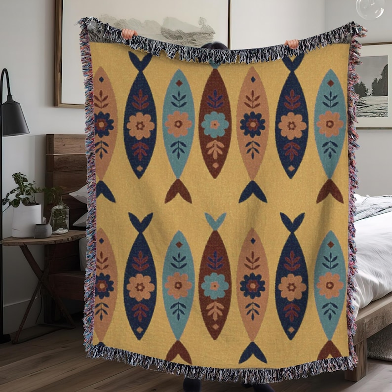 May include: A yellow throw blanket with a repeating pattern of stylized fish. Each fish has a dark blue tail and is decorated with floral and leaf motifs in shades of brown, blue, and orange. The blanket has a fringed edge.
