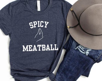 May include: A navy blue t-shirt with the text "Spicy Meatball" in white lettering. The text is accompanied by a white hand gesture, commonly known as the "Italian hand gesture".