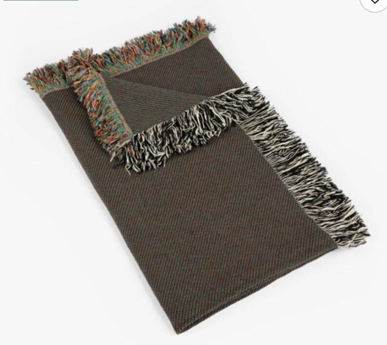 May include: A green and brown woven throw blanket with a black and white fringe border. The blanket has a textured weave and is folded in half.