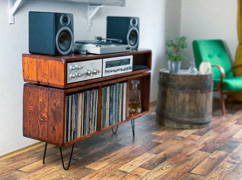 May include: A wooden record player stand with a record player, two speakers, and a shelf for vinyl records. The stand has a dark brown finish and is on black hairpin legs.