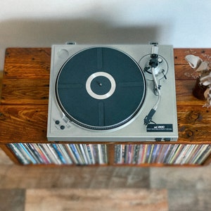 May include: A silver record player with a black turntable on a wooden stand with a shelf full of vinyl records.