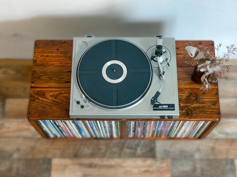 May include: A silver record player with a black turntable on a wooden stand with a shelf full of vinyl records.