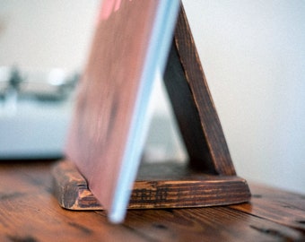 May include: A wooden record stand with a dark brown finish, holding a pink and blue vinyl record.