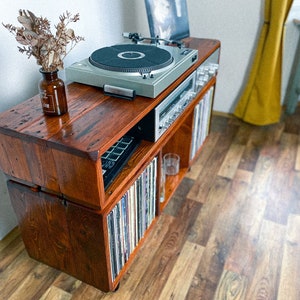 May include: A wooden record player stand with a turntable, amplifier, and shelves for vinyl records. The stand is made of reclaimed wood and has a rustic look.