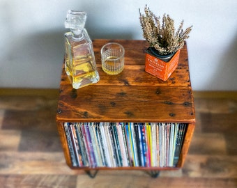 May include: A wooden record player stand with a shelf for displaying items. The stand has a clear glass decanter with a stopper, a glass, and a small tin with dried flowers and the text "Twinings English Breakfast Tea" on it.