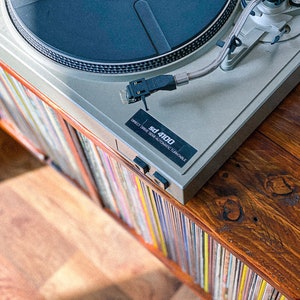 May include: A silver turntable with a black platter and a silver tonearm. The turntable is labeled "sd 4100 Direct Drive Semi-Automatic Turntable". The turntable is sitting on a wooden shelf with a collection of vinyl records.