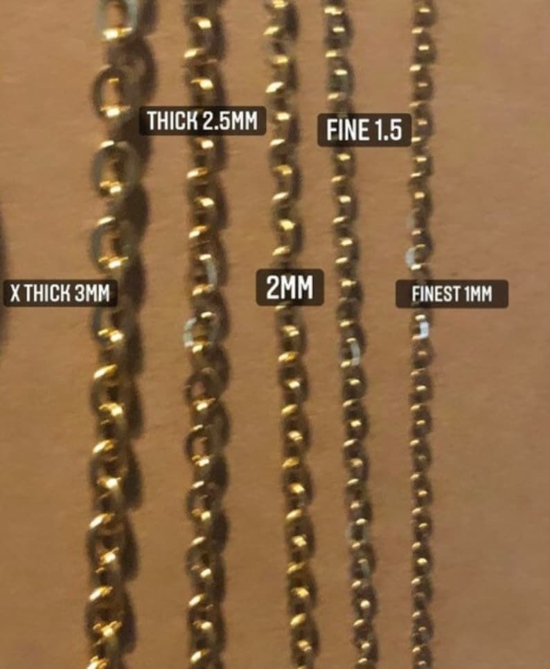K&ouml;nnte beinhalten: F&uuml;nf goldene Ketten in verschiedenen St&auml;rken, beschriftet mit ihren Ma&szlig;en in Millimetern. Die Ketten sind von der dicksten zur d&uuml;nnsten angeordnet, wobei die dickste Kette mit "X THICK 3MM" beschriftet ist, gefolgt von "THICK 2.5MM", "2MM", "FINE 1.5" und "FINEST 1MM".