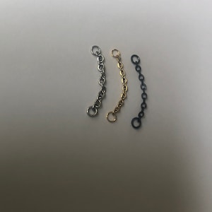 K&ouml;nnte beinhalten: Drei silberne, goldene und schwarze Kettenverl&auml;ngerungen. Jede Verl&auml;ngerung ist etwa 5 cm lang und hat an jedem Ende eine Schlaufe.