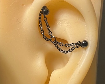 Könnte beinhalten: Schwarzer Ketten-Barbell-Ohrring mit zwei schwarzen Perlen. Der Ohrring wird in einem Helix-Piercing getragen.