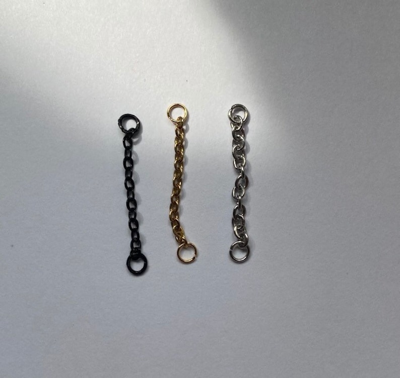 K&ouml;nnte beinhalten: Drei Kettenverl&auml;ngerungen in Schwarz, Gold und Silber. Jede Verl&auml;ngerung hat zwei Sprungringe an den Enden.