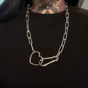 May include: A silver chain necklace with a heart-shaped clasp. The chain is made of linked oval shapes.