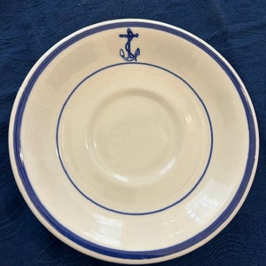 May include: White ceramic saucer with a blue rim and a blue anchor design in the center.