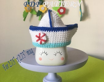 May include: White crocheted sailor hat with blue trim and a red and white life preserver design. The hat is sitting on a white mug with a smiley face. The text "For 2.75" x 2.75" mug" is written below the mug.