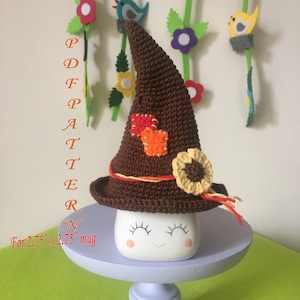 May include: Crochet hat pattern for a 2.75 inch mug. The hat is brown with a yellow flower and orange and red squares. The pattern is called "PDF PATTERN".