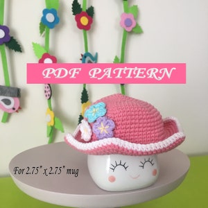 May include: A pink crocheted hat with white trim and colorful flower embellishments. The hat is designed to fit a 2.75" x 2.75" mug.  PDF PATTERN.