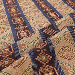 May include: Close-up of a fabric with a brown, blue, and gold geometric pattern. The fabric has a woven texture and is folded in half.