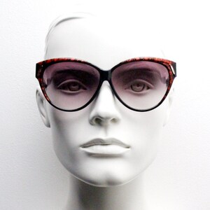 Puede incluir: Un maniquí con gafas de sol de ojo de gato negras y rojas con lentes de degradado marrón.