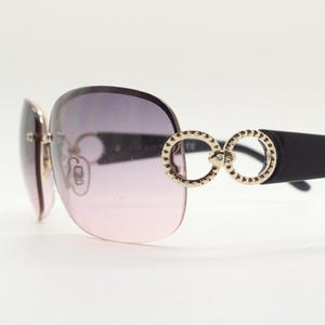 May include: Black sunglasses with a pink gradient lens and gold-toned double circle accents on the bridge.