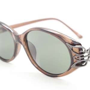 Occhiali da sole ovali a forma di occhio di gatto vintage anni &#39;90. Montatura da donna a forma di occhio di gatto, marrone trasparente, dal profilo basso, con angoli decorativi in metallo. Occhiali a forma di occhio di gatto, mai usati e nuovi di zecca.