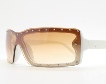 May include: White sunglasses with a brown gradient lens and rhinestones around the frame.