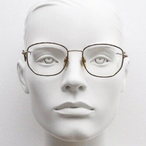 May include: A white mannequin head wearing a pair of gold-rimmed glasses with square lenses.