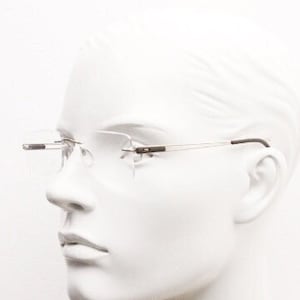 May include: A rimless pair of eyeglasses with a silver frame and clear lenses. The glasses are on a white mannequin head.