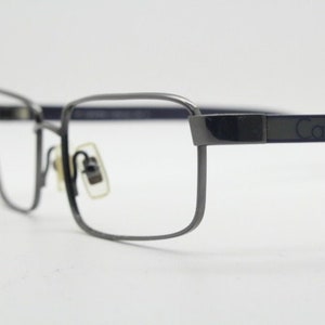 May include: Silver-toned metal eyeglasses with a dark gray Calvin Klein logo on the temple arm.