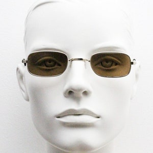 May include: A white mannequin head wearing a pair of gold-rimmed sunglasses with brown lenses.