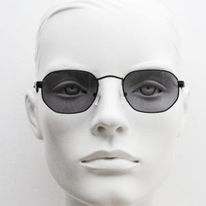 May include: A white mannequin head wearing black square-shaped sunglasses with dark gray lenses.