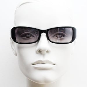 May include: Black rectangular sunglasses with gradient lenses. The sunglasses have a thick, rounded frame and are displayed on a white mannequin head. The lenses transition from dark at the top to lighter at the bottom.