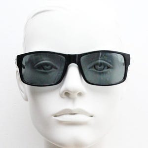 Y2K vintage scharfe rechteckige Sonnenbrille. Großer geschwungener schwarzer Glanzrahmen mit dunkelgrünen Gläsern und silbernen Pfeilarmspitzen. nr