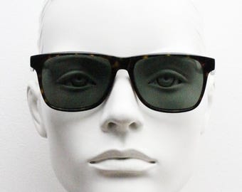 Wyrafinowane, prostokątne okulary przeciwsłoneczne Bailey Nelson Wayfarer. Klasyczny, ponadczasowy format vintage. Ręcznie wykonana, ciemna oprawka w kolorze szylkretowym z zielonymi soczewkami.
