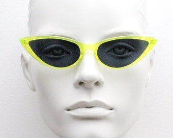 Vintage Y2K zonnebril met extreem spitse cat-eye vorm. Gestileerd geel transparant montuur met zwarte glazen. Dames zonnebril in psychabilly stijl uit de jaren 50. Nieuw in doos.