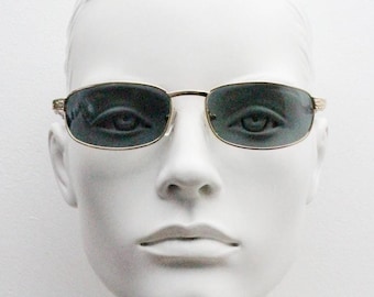 Gafas de sol rectangulares doradas de perfil bajo vintage de los años 90. Montura de metal macizo con acabado cromado brillante, diseño en relieve en las patillas y lentes verdes. NOS