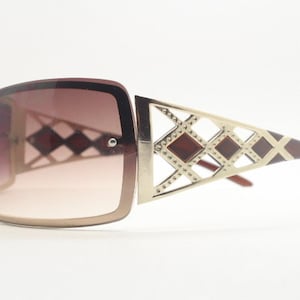 May include: Brown and gold sunglasses with a geometric design on the frame. The lenses are brown and gradient.