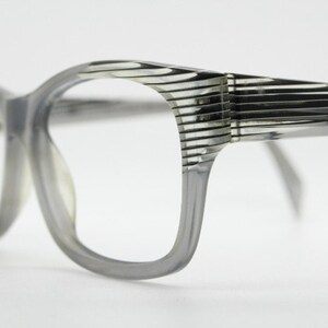 Puede incluir: Gafas de plástico gris con marco y un patrón de rayas en las patillas.