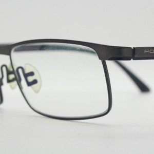 May include: Black metal frame eyeglasses with clear lenses. The frame has the text "PORSCHE DESIGN" on the side.