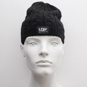 May include: Black knitted beanie with a cable knit pattern and a black UGG Australia logo patch.